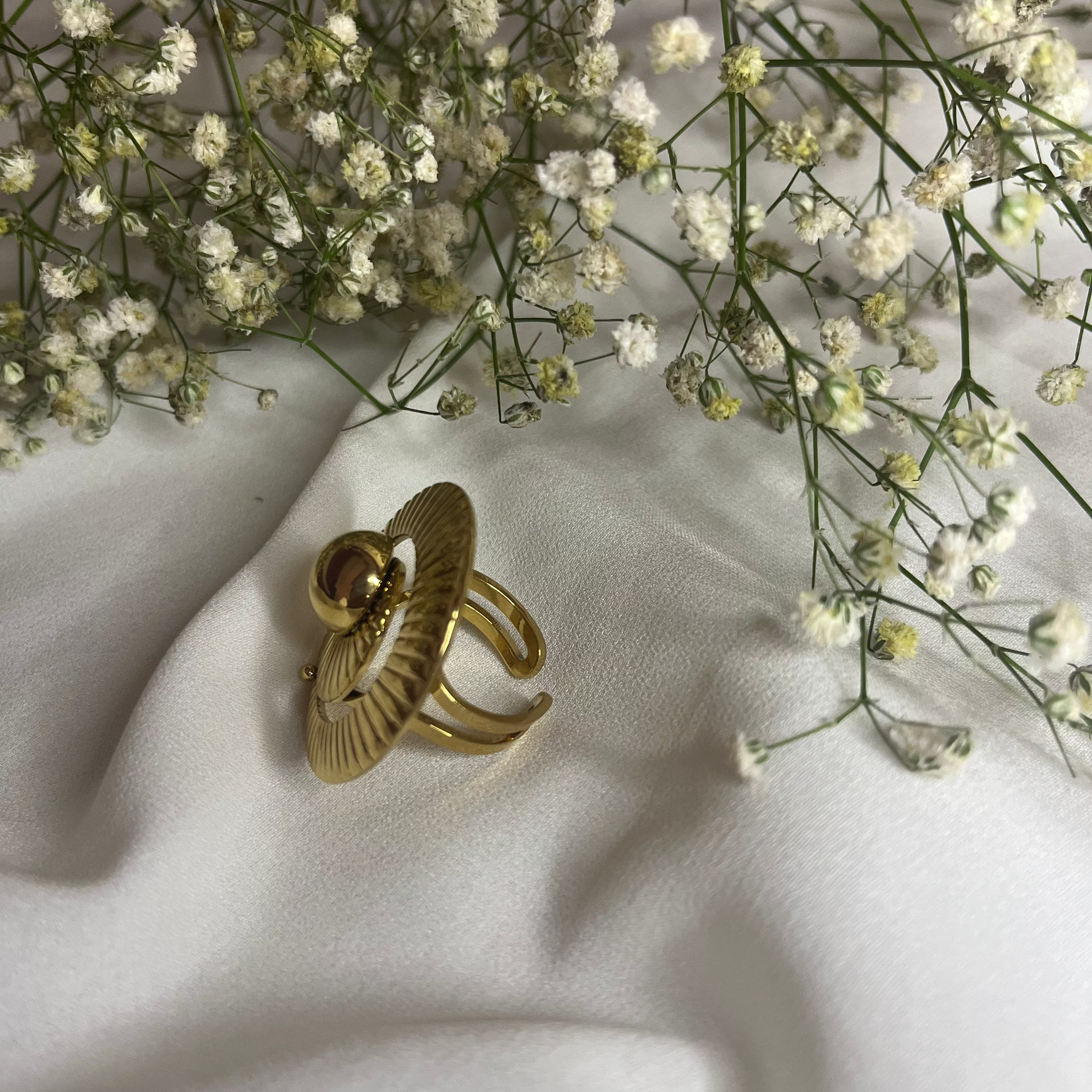 Gold ring with a decorative design on a white fabric background with small white flowers.