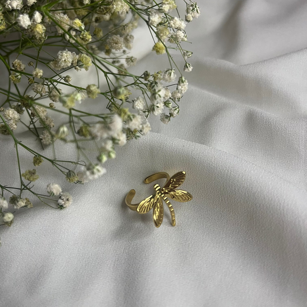 Gold bee-shaped brooch on a white fabric background with small white flowers.