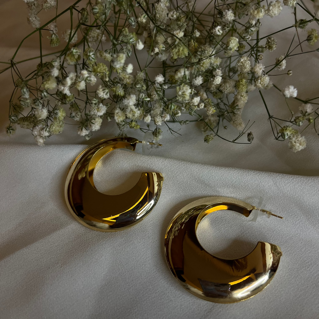 Gold hoop earrings on a white surface with small white flowers in the background