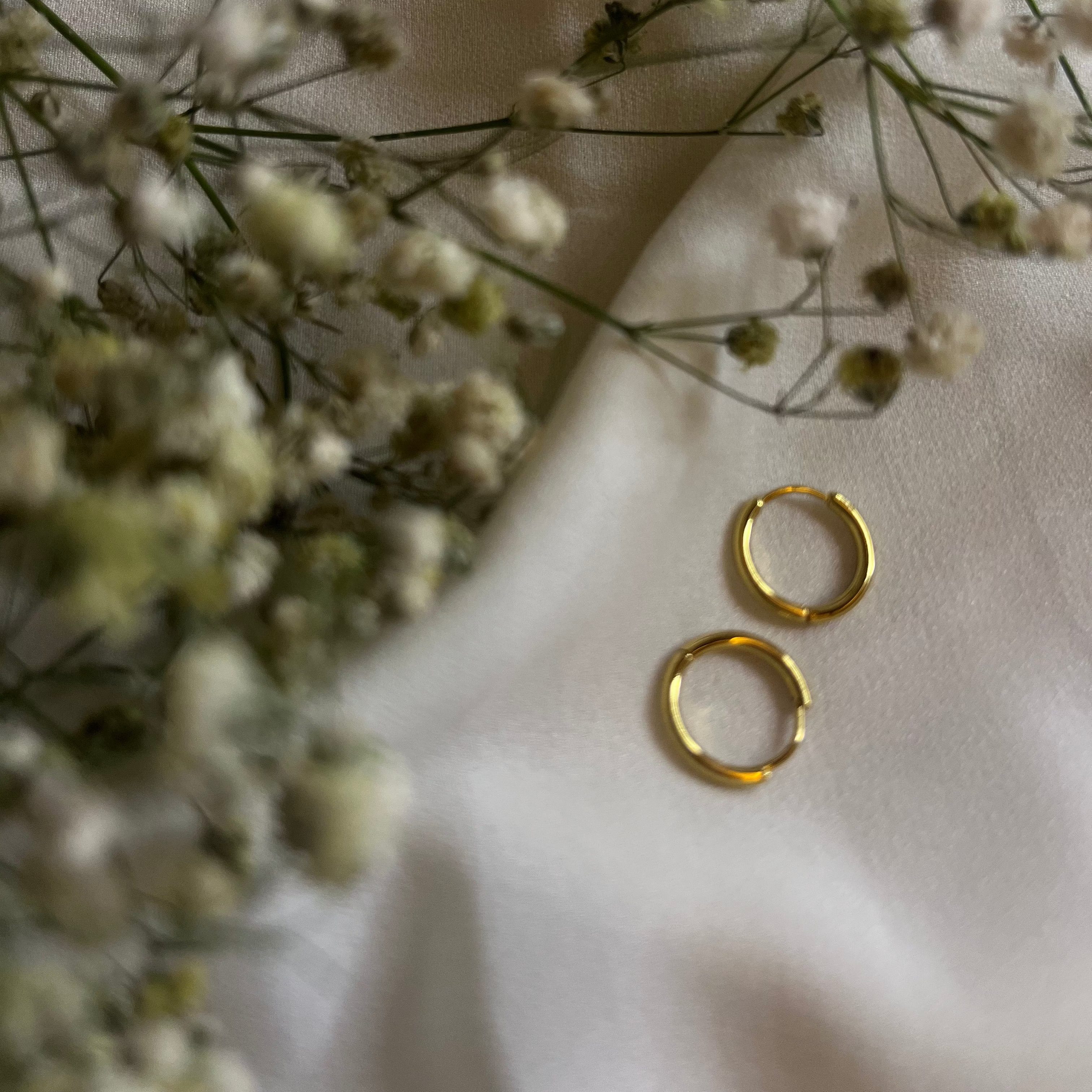 Gold hoop earrings on a light fabric background with small white flowers.