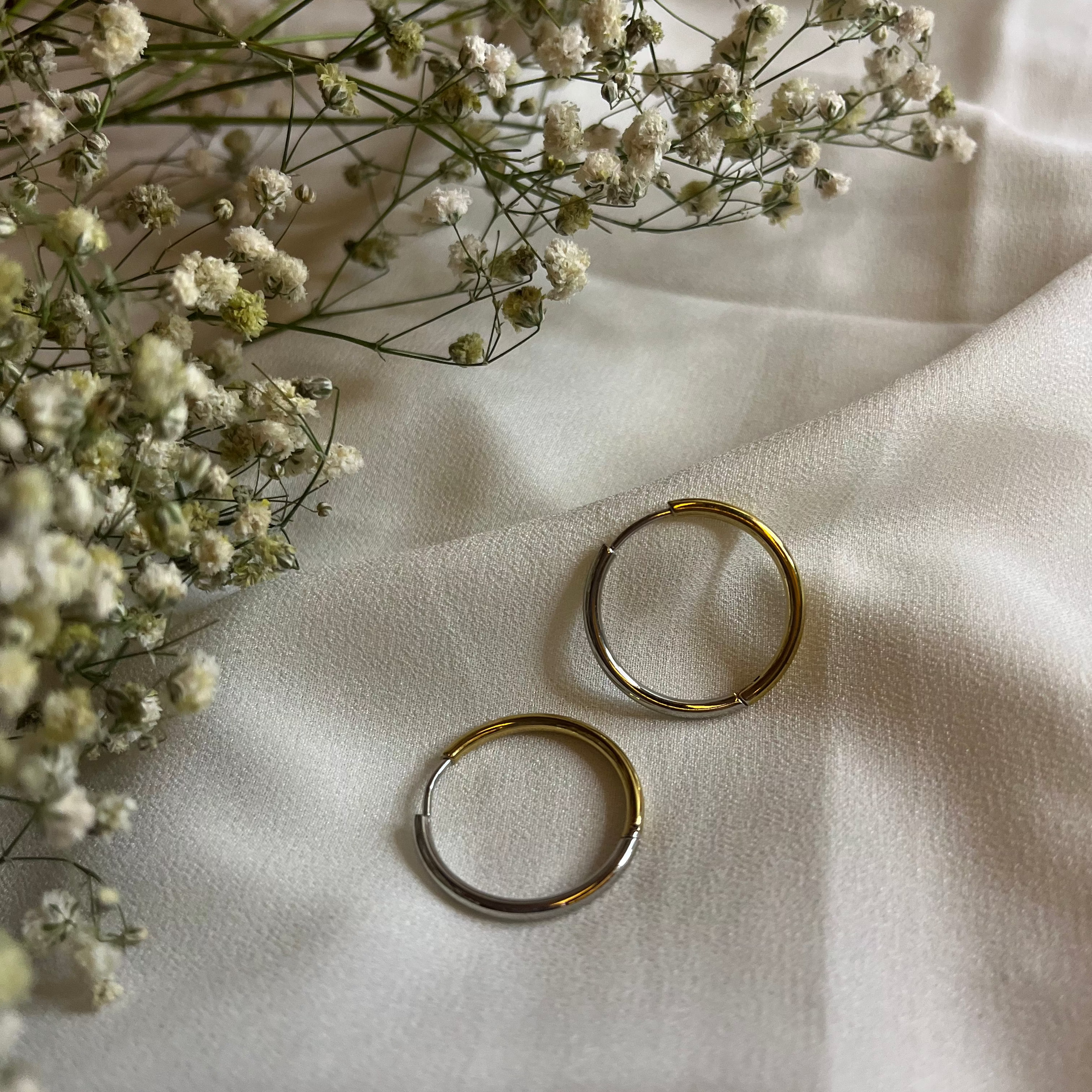 Hand holding two gold rings with a soft background of flowers and fabric