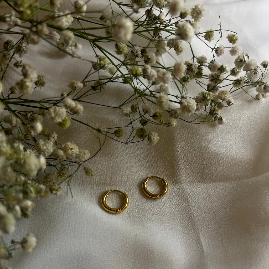 Gold hoop earrings on a white fabric background with small white flowers.