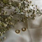 Gold hoop earrings on a white fabric background with small white flowers.