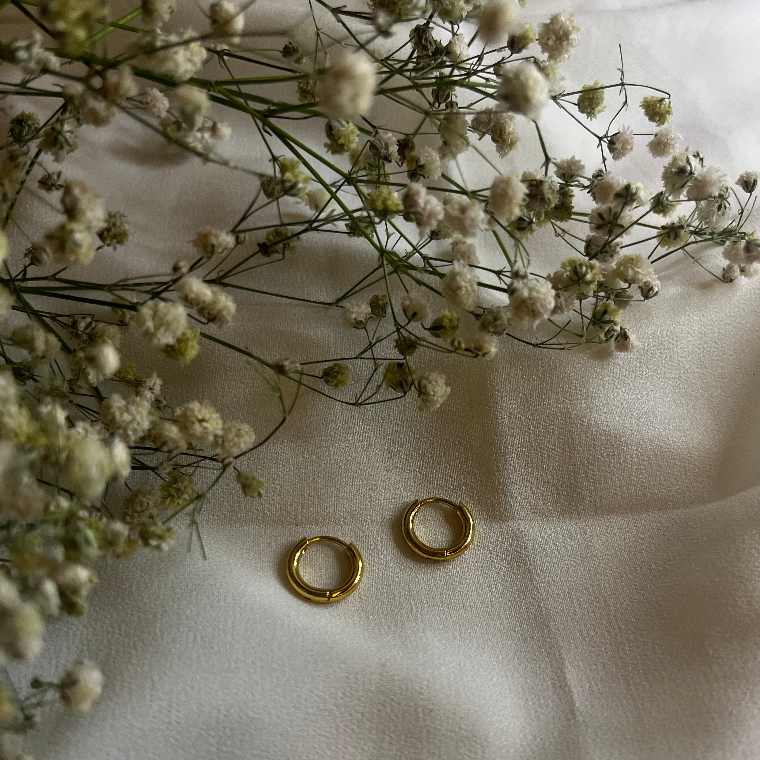 Gold hoop earrings on a white fabric background with small white flowers.